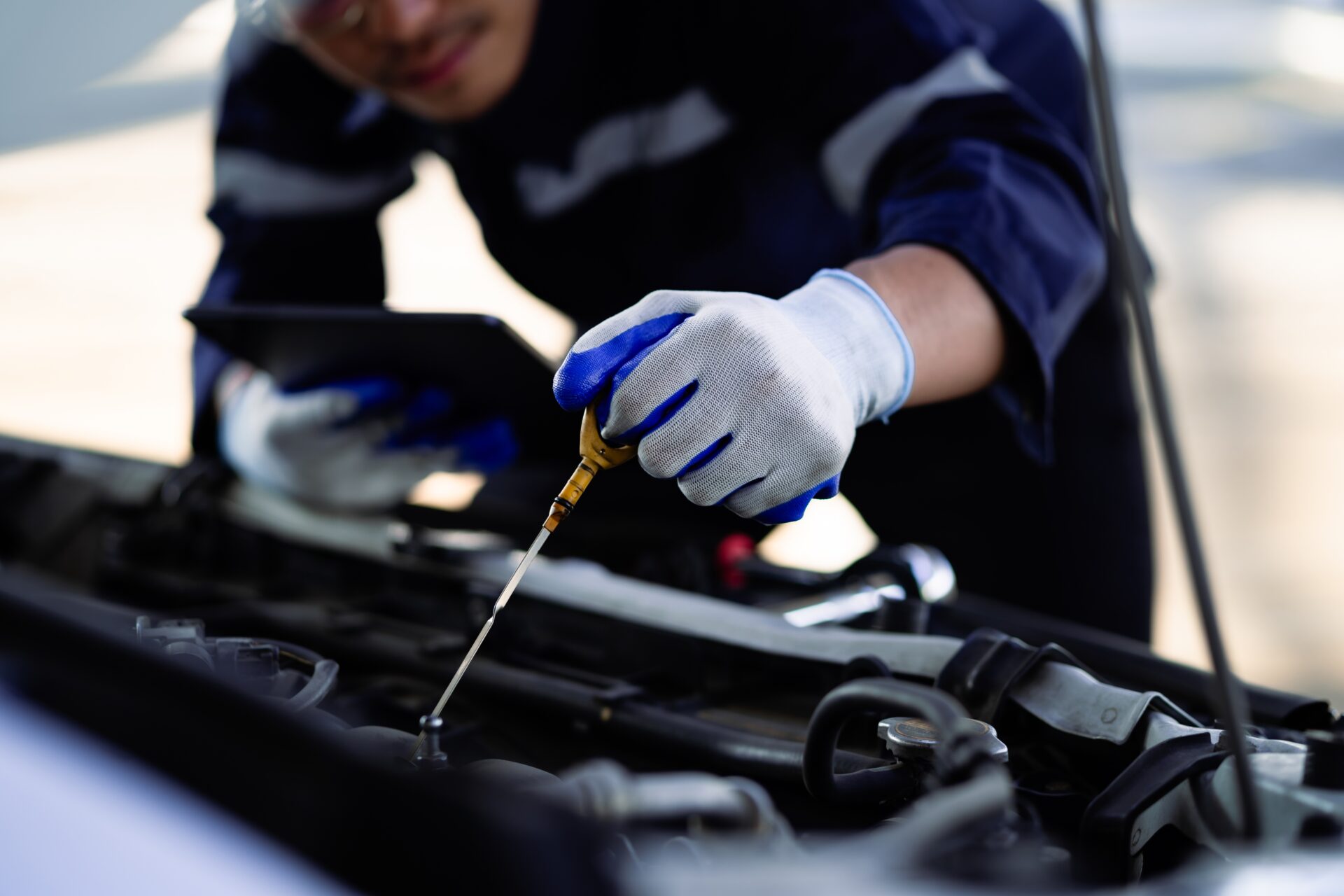 A mechanic is checking the oil in a car. The oil is low and the mechanic is adding more