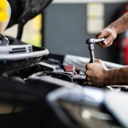Caucasian Male Mechanic Repairs Car In Garage. Car Maintenance And Auto Service Garage Concept. Closeup Hand And Spanner.